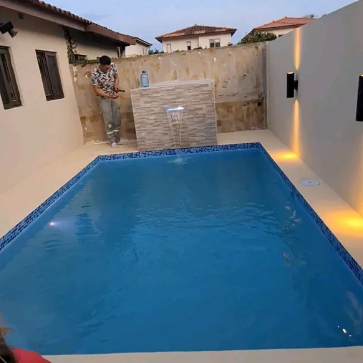 Piscina con muro de fuentes revestido en piedra e iluminación cálida